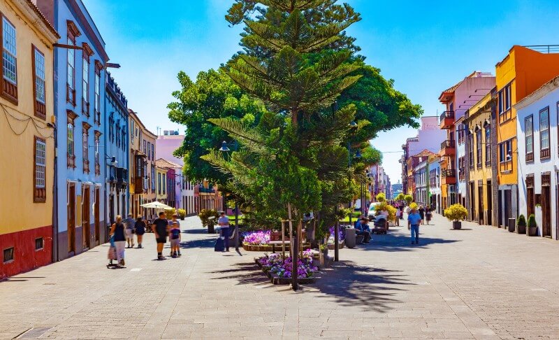 Colourful colonial street in San Cristóbal de La Laguna, Tenerife, with people walking under bright sunlight.